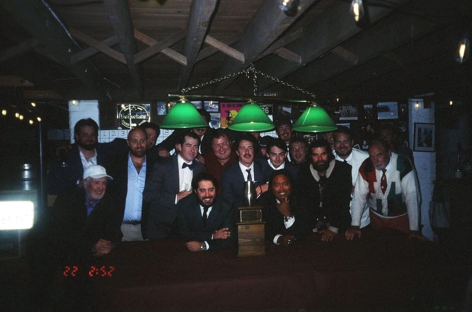 The full field in jackets and ties around the trophy at the basement bar